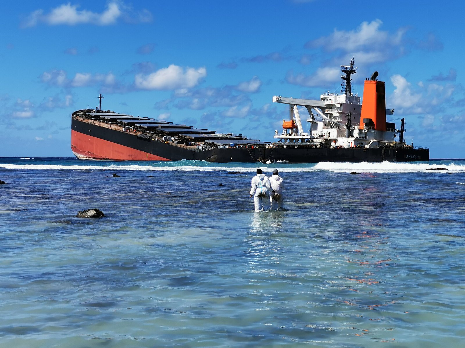 International Maritime Organization (IMO) workers in hazmat suits stand in surf near the wreck of the MV Wakashio on August 13, 2020.